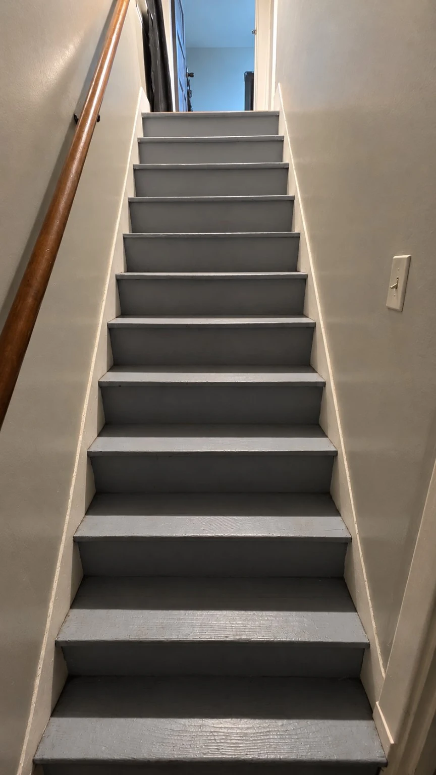 Gray painted staircase with a wooden handrail leading upstairs in Raven's family home