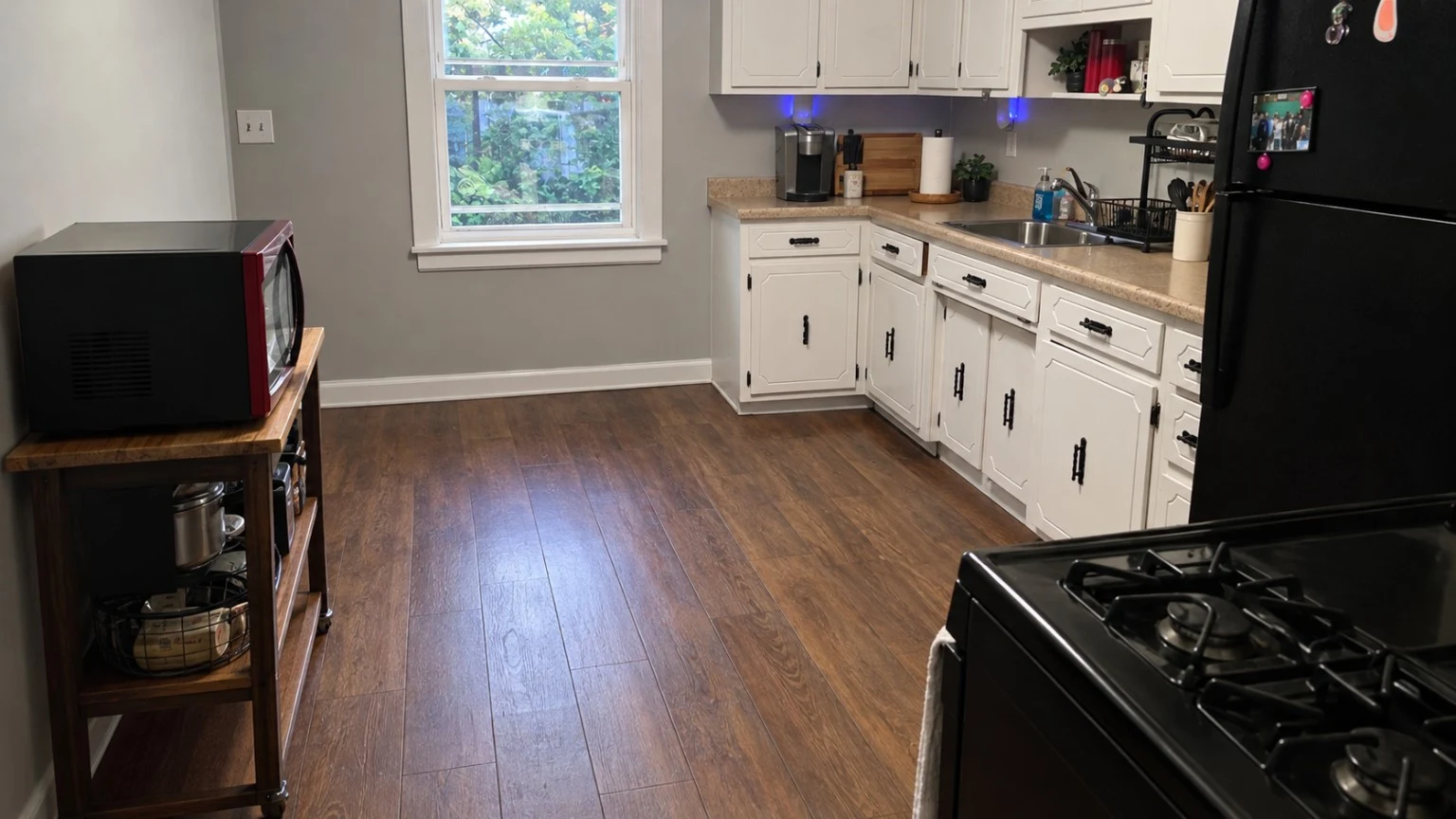 Another view of Raven's kitchen with white cabinets, a window and open wood floors