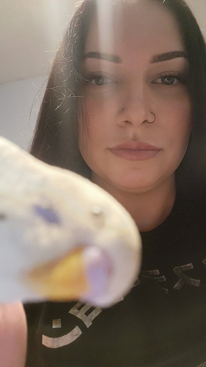 Sora the beloved parakeet, very close to the camera with Raven smiling behind him