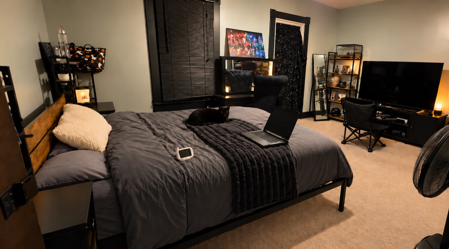 Upstairs bedroom with a neatly made bed, comfortable seating, television and a resting black cat